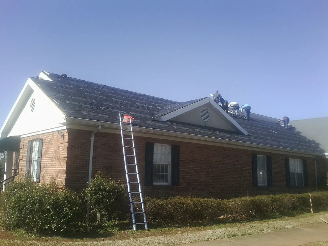 Crew tearing shingles off a brick ranch roof with a ladder set — Emergency Roof Repair work by our crew in Rollinsford