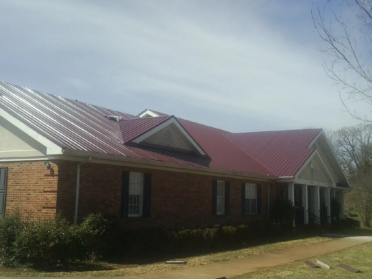 Red metal roof with gabled entries on a long brick building, from a Hail Damage Roof Repair job in Rollinsford