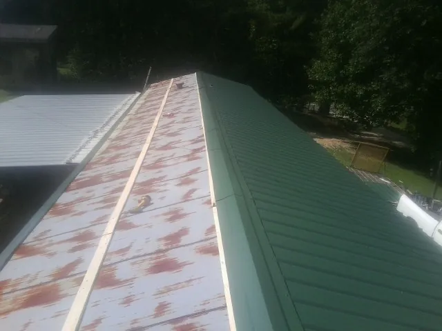 Old rusted panels beside newly installed green metal roofing — Wind Damage Roof Repair by Roofing Brothers in Rollinsford