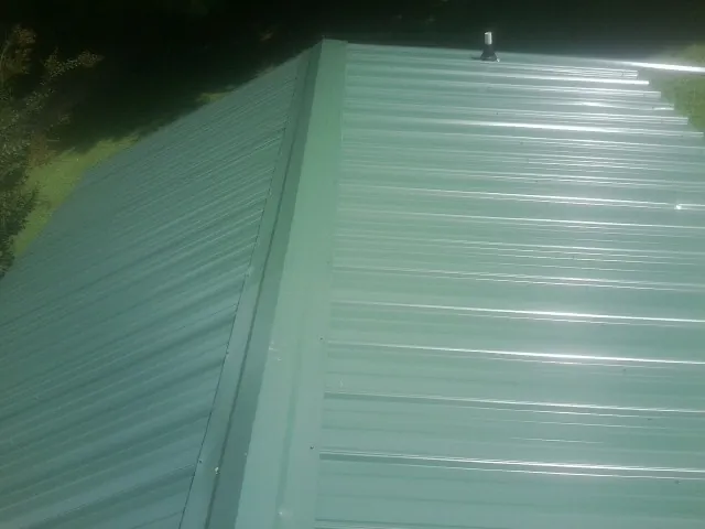 New green metal panels meeting at the ridge of a roof — Flat Roof Repair work by our crew in Rollinsford