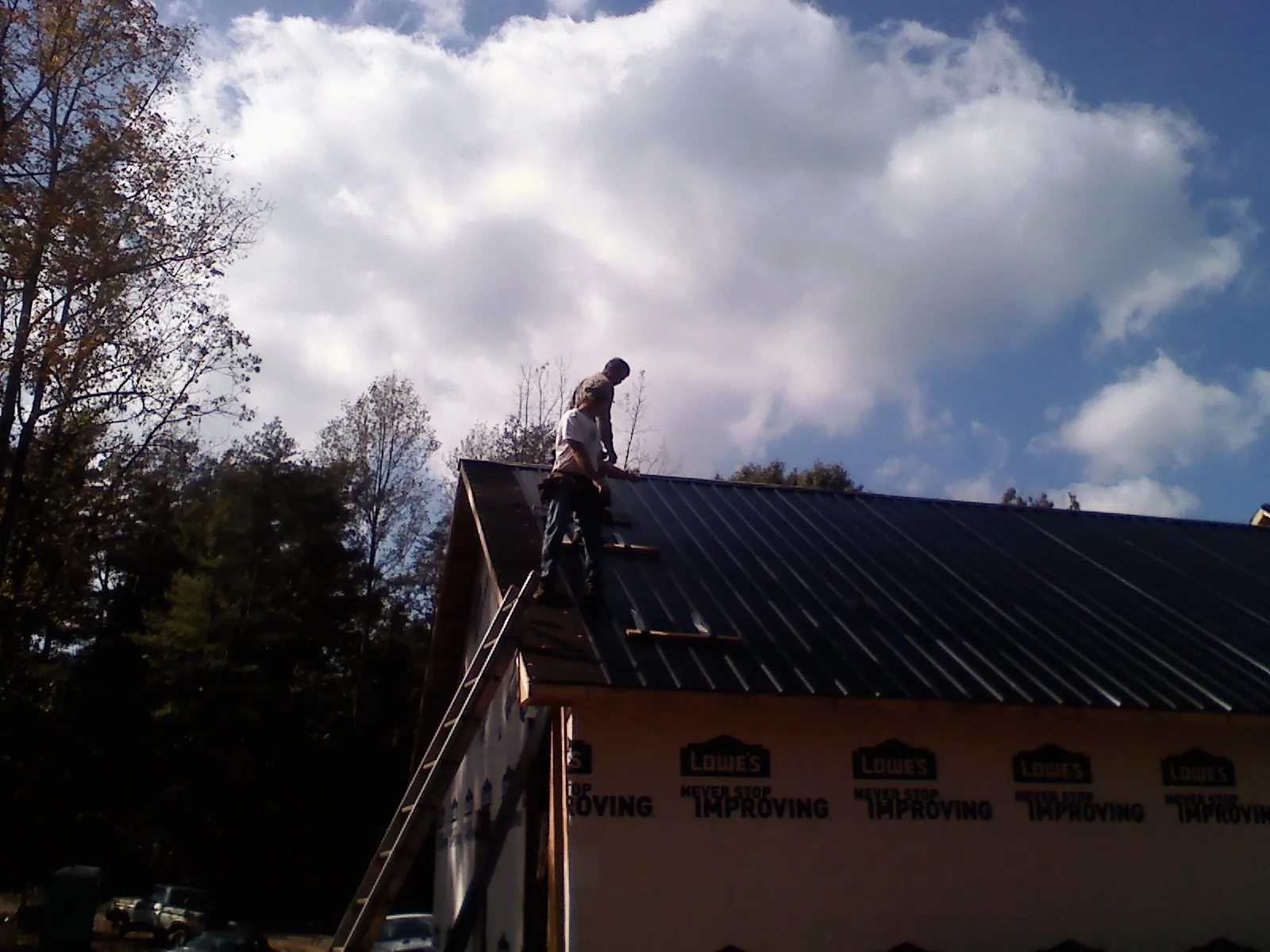 Roofer fastening dark metal panels high against a cloudy sky, from a Roof Inspection job in Rollinsford