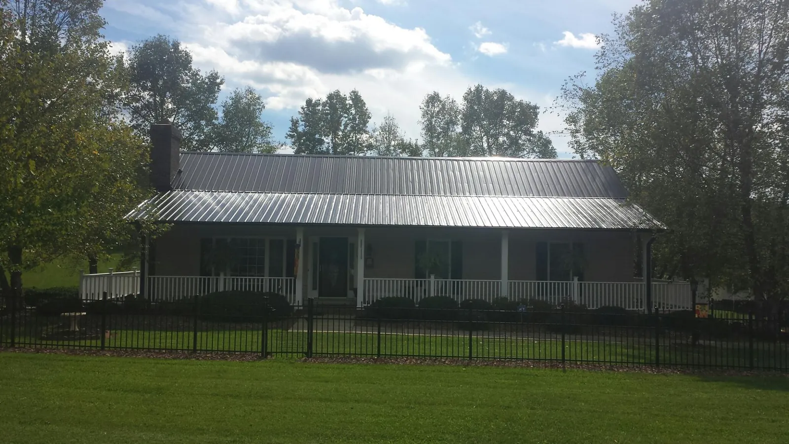 Gray metal roof on a brick ranch with a full width front porch — Gutter Guard Installation work by our crew in Rollinsford