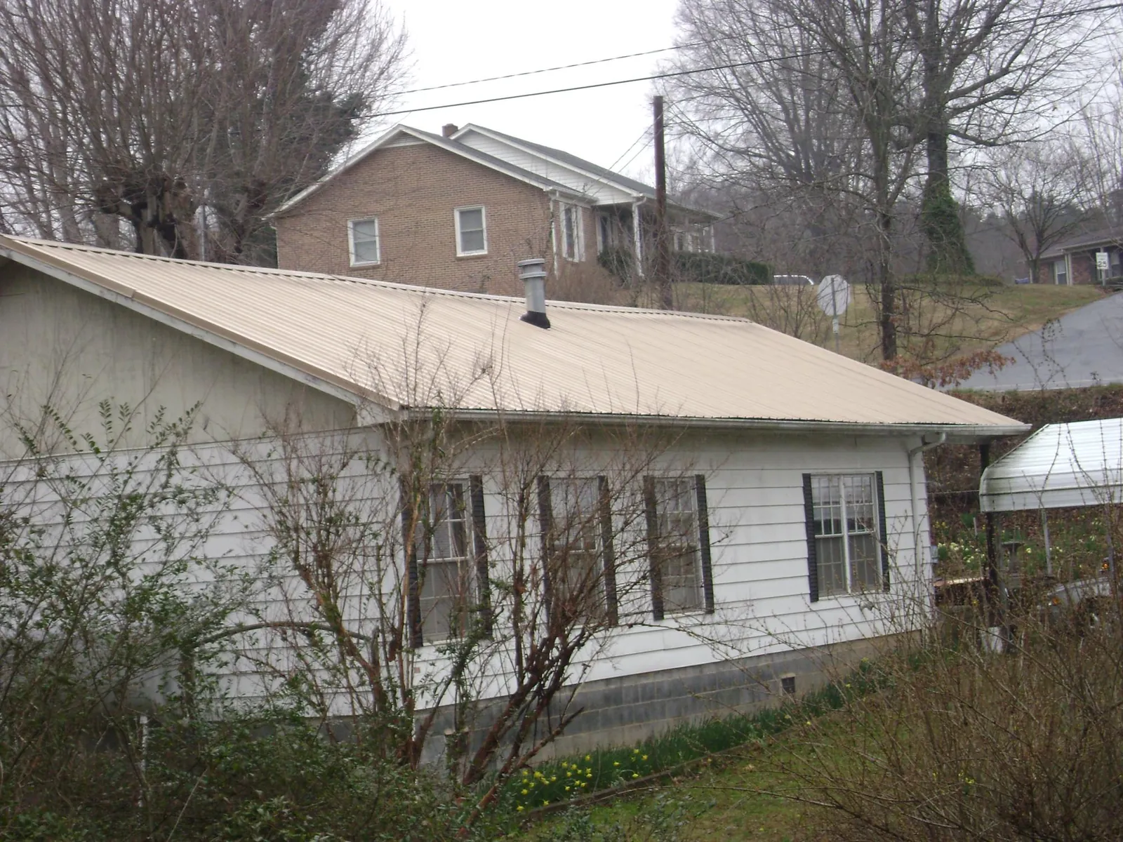 Tan metal roof on a white sided house set into a hillside — Commercial Roofing by Roofing Brothers in Rollinsford