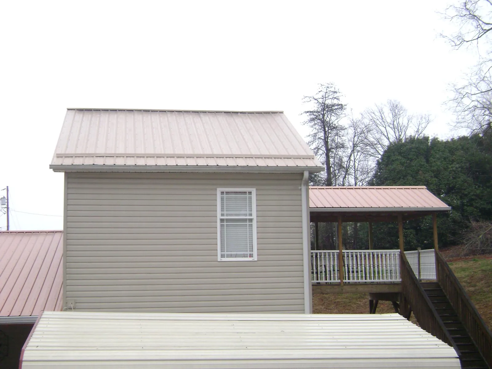 Tan metal roofs on a two story addition and attached porch, from a Roof Replacement job in Rollinsford